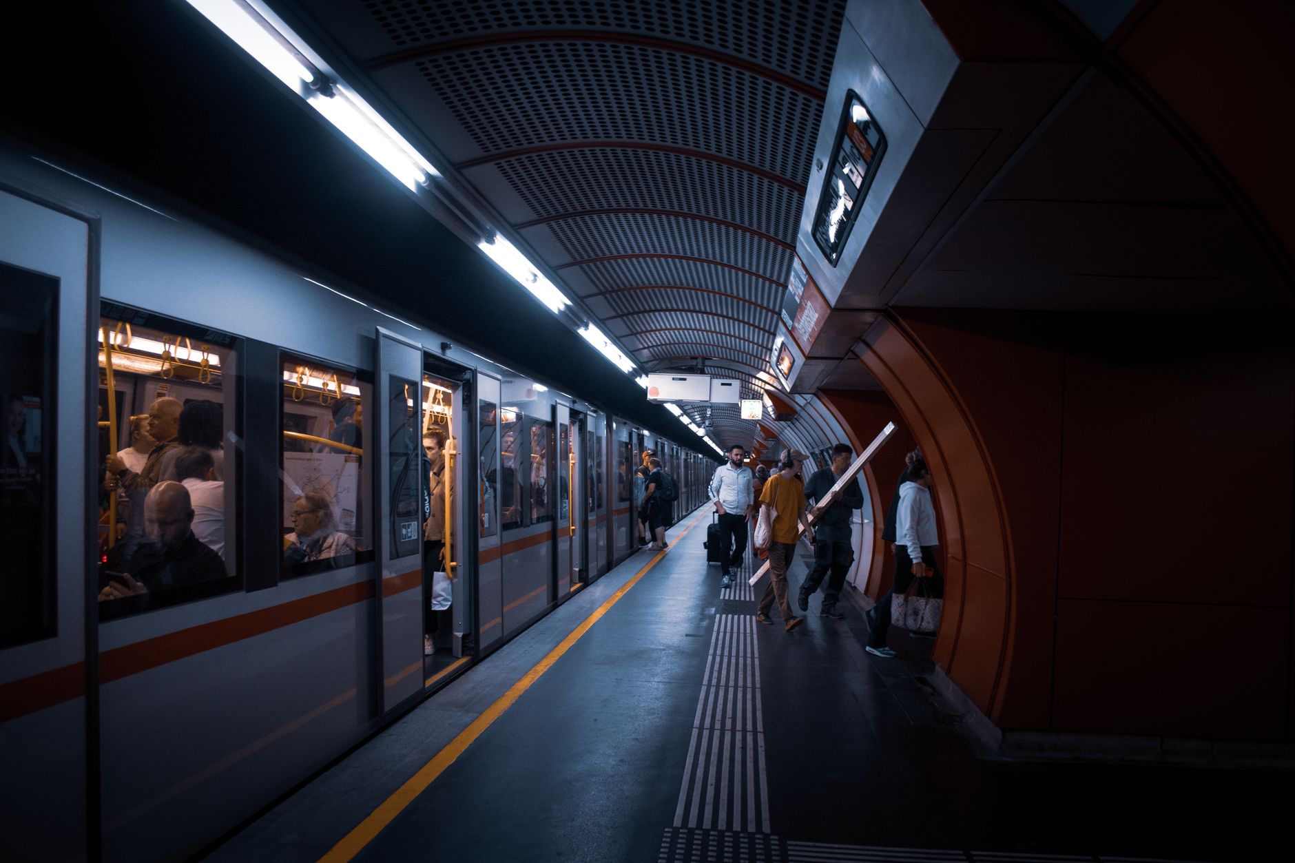A modern subway station bustling with evening commuters boarding and exiting trains.