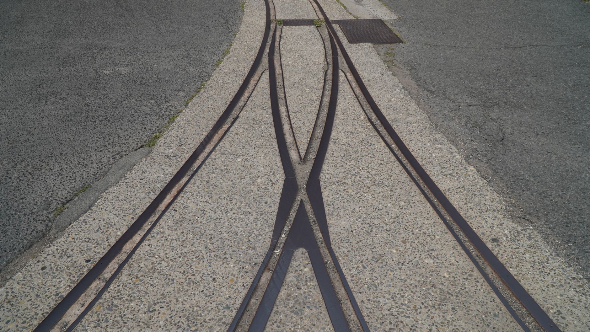 Close-up view of intersecting steel rail tracks embedded in concrete pavement.