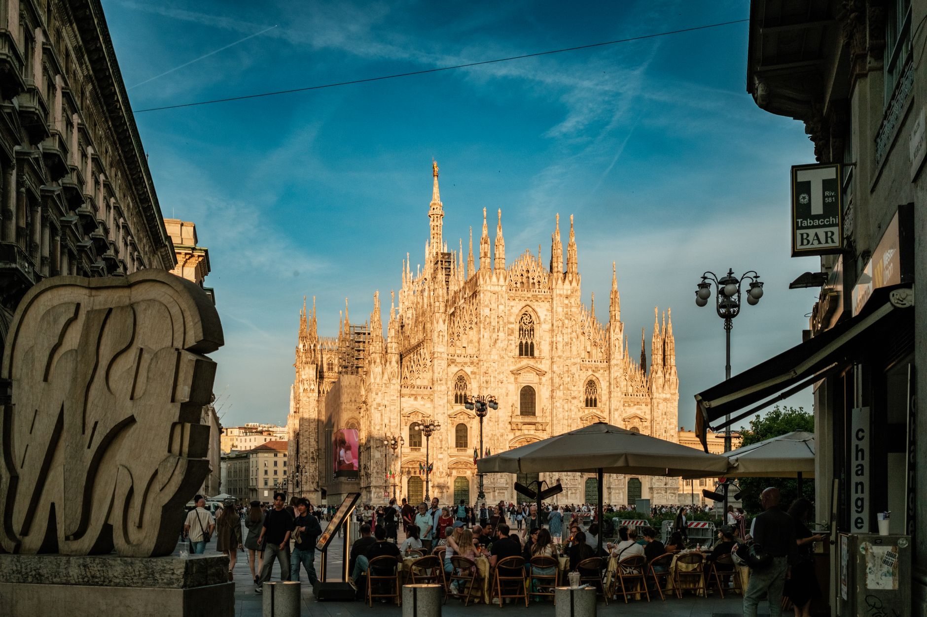 Enjoy a lively evening scene at the Duomo di Milano with bustling crowds and beautiful architecture.