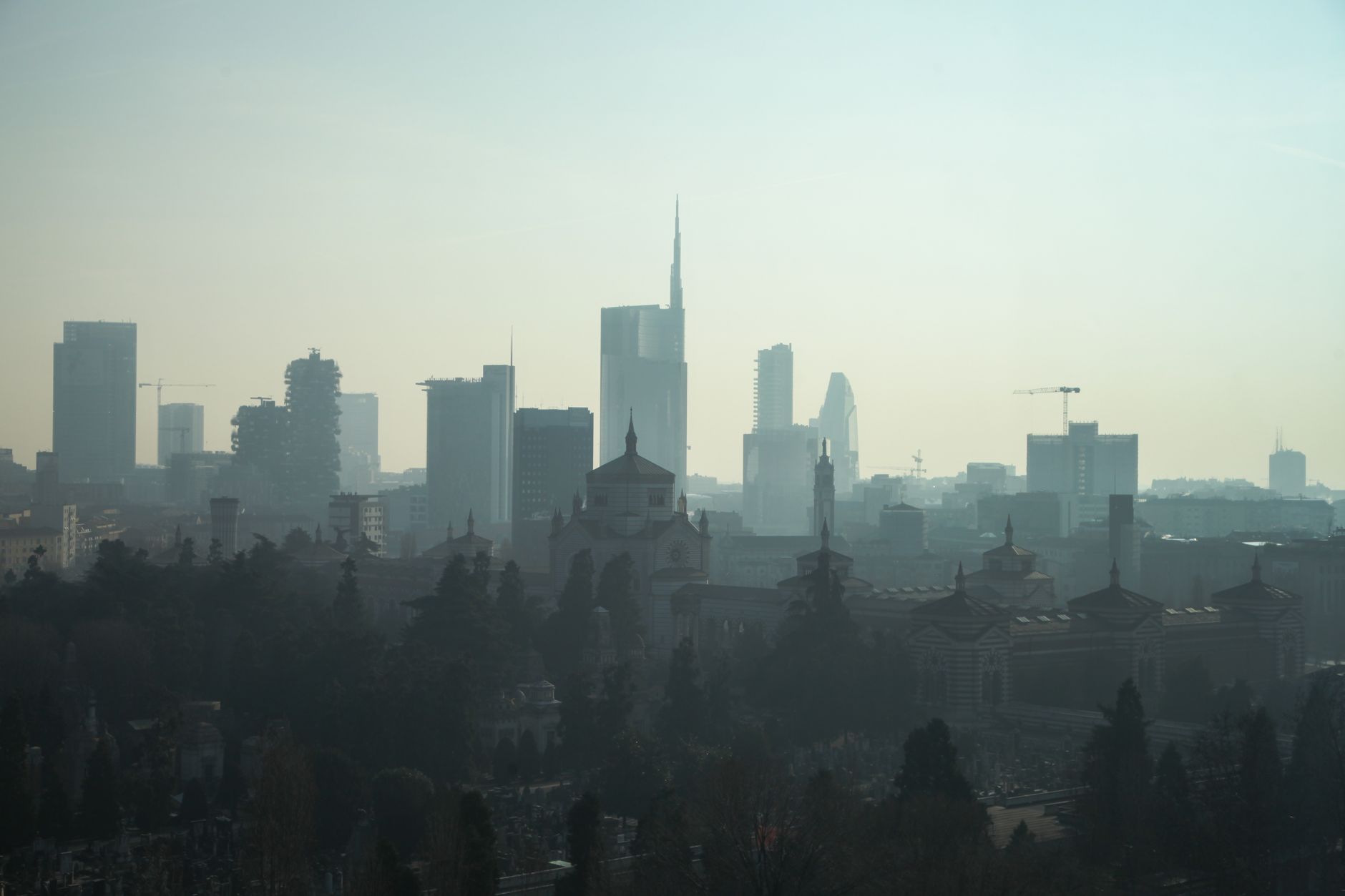 A foggy view of the Milan cityscape with modern skyscrapers and historic architecture.
