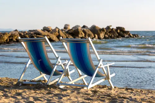Two striped beach chairs facing the calm ocean waves on a sunny day, offering a tranquil beach escape.