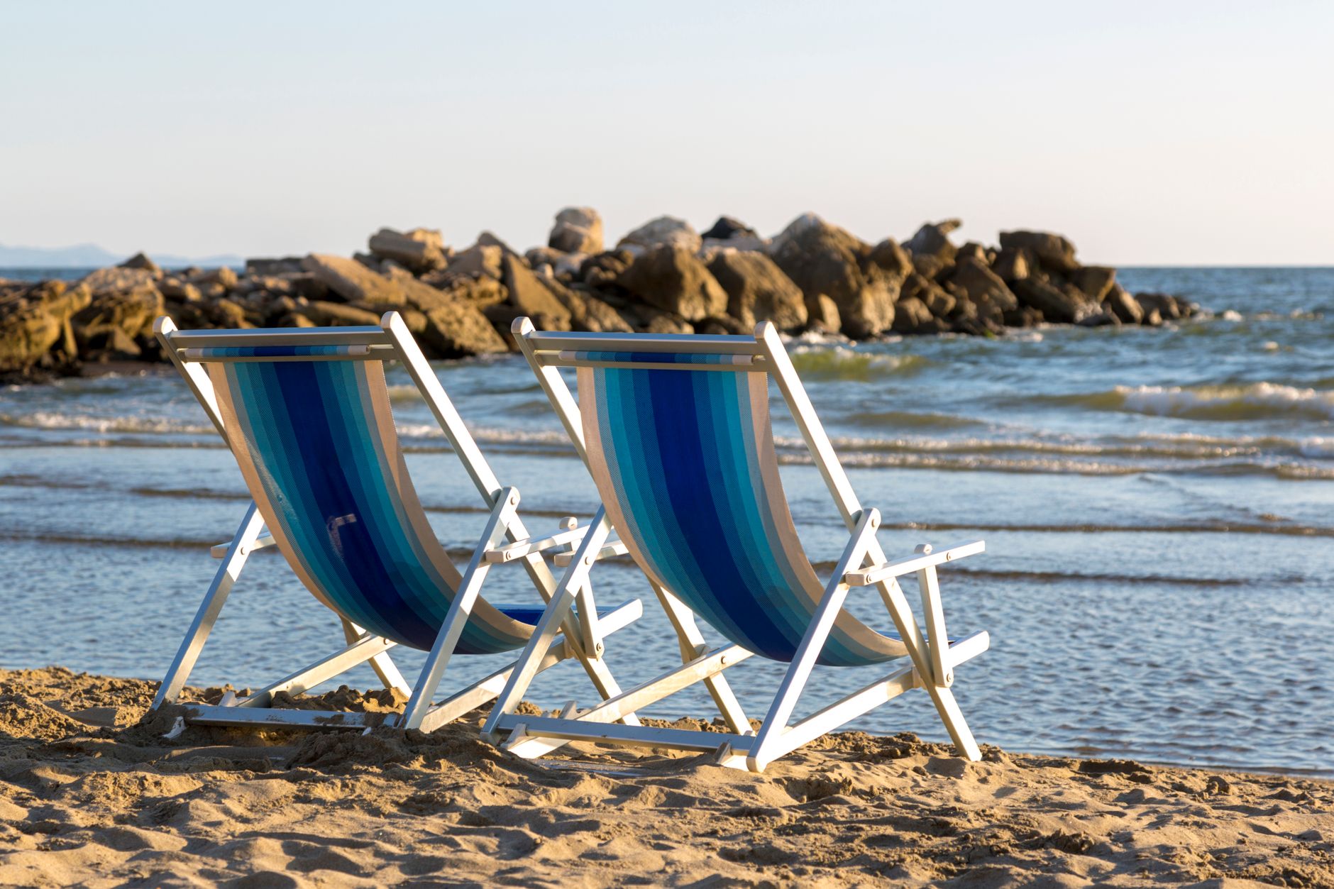 Two striped beach chairs facing the calm ocean waves on a sunny day, offering a tranquil beach escape.
