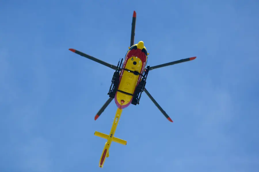 Vibrant yellow rescue helicopter soaring with rotors spinning against a clear blue sky.