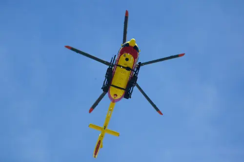Vibrant yellow rescue helicopter soaring with rotors spinning against a clear blue sky.