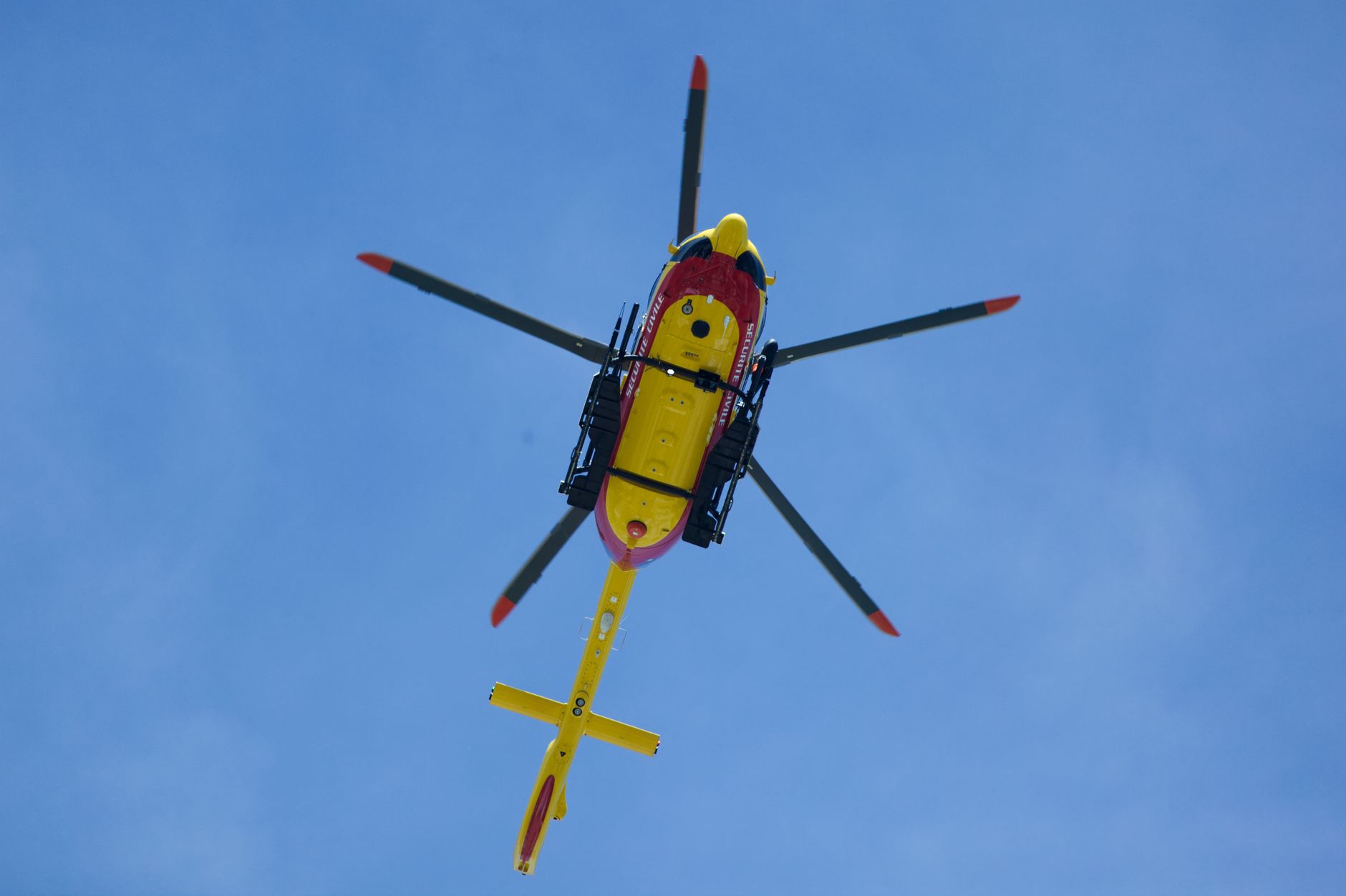 Vibrant yellow rescue helicopter soaring with rotors spinning against a clear blue sky.