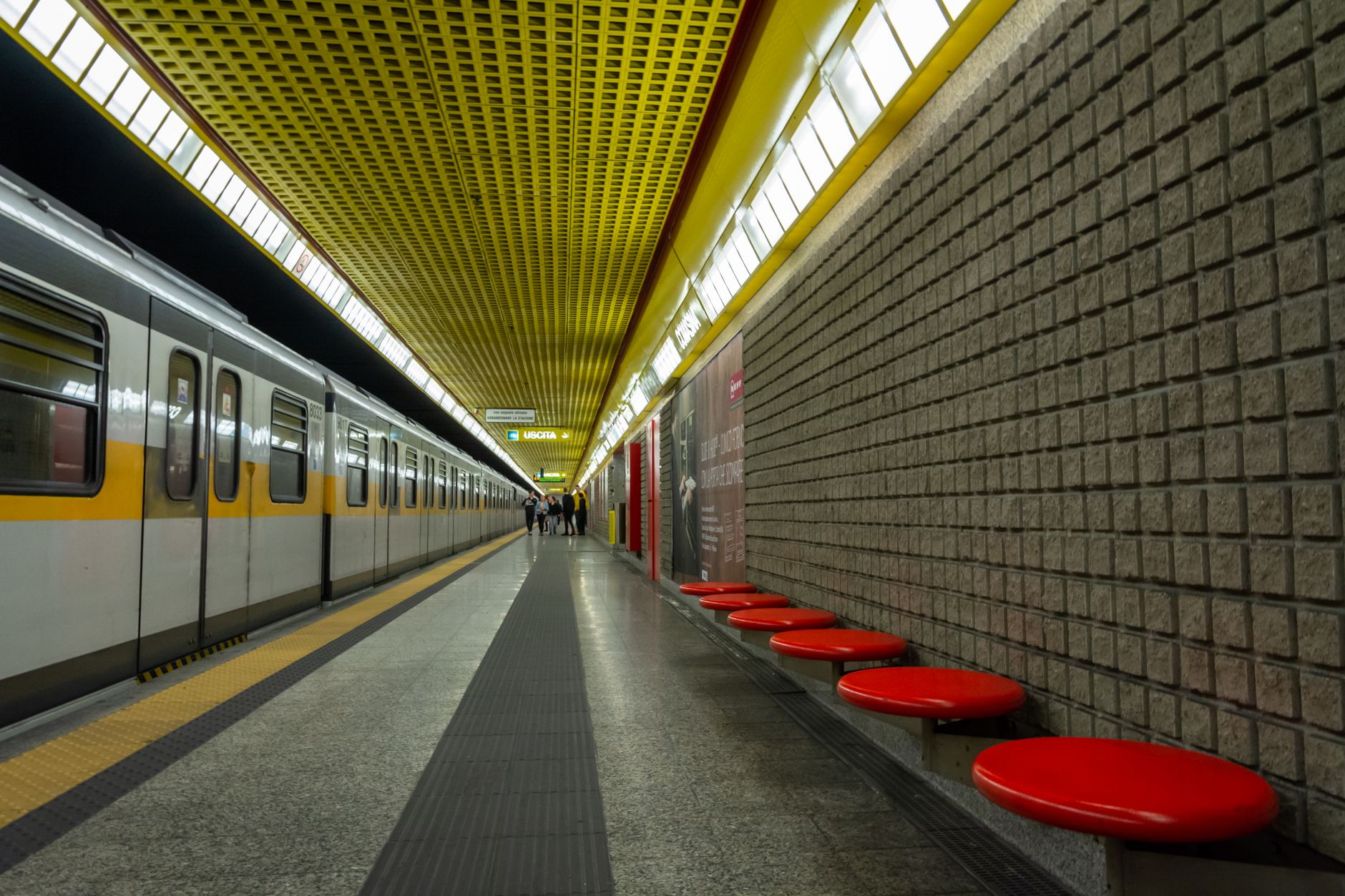 Empty subway platform with yellow ceiling and red benches, modern design.