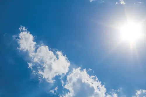 A clear blue sky with fluffy clouds and bright sunshine, representing a perfect summer day.