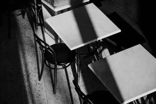 Black and white image of café tables and chairs with striking shadows.