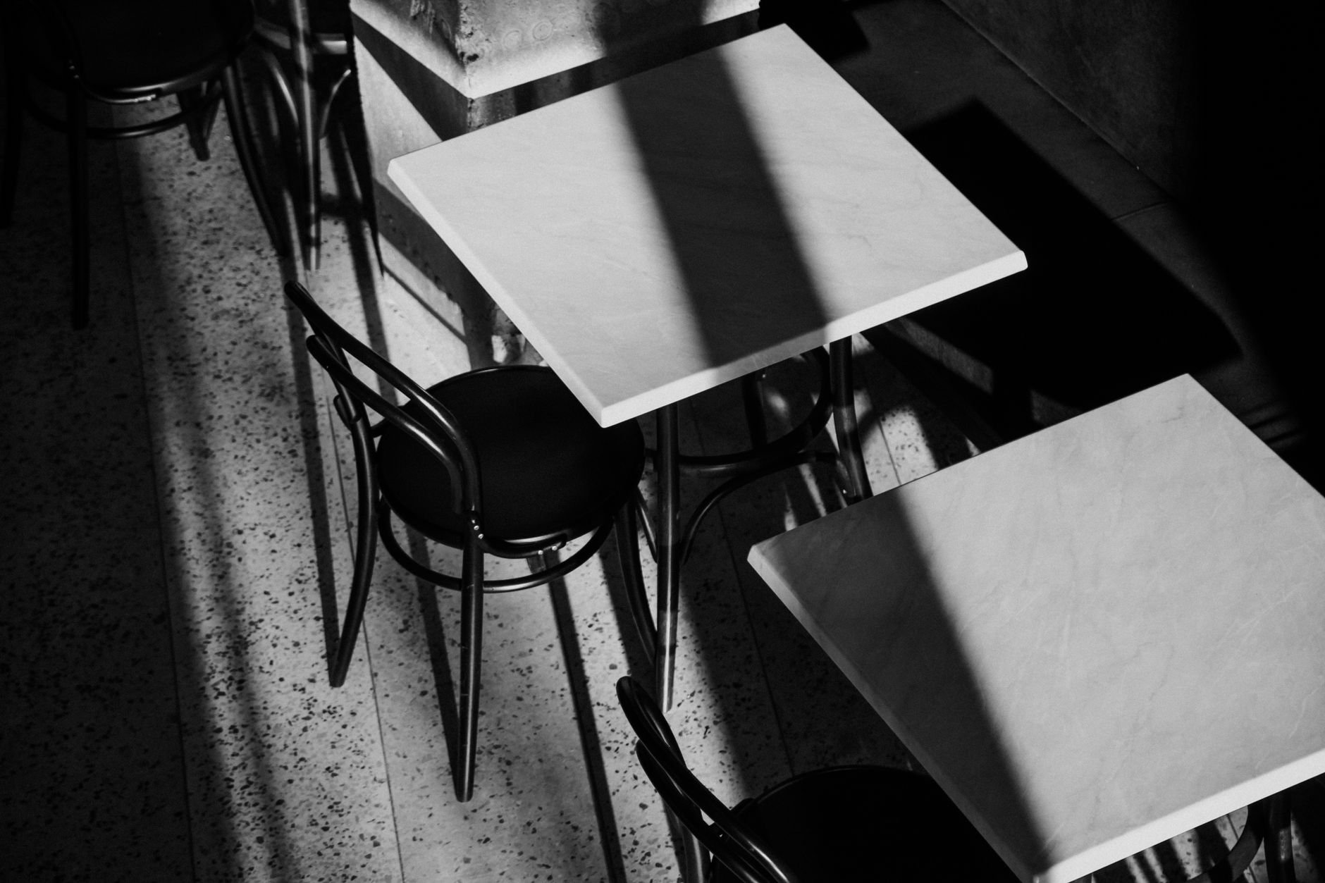 Black and white image of café tables and chairs with striking shadows.