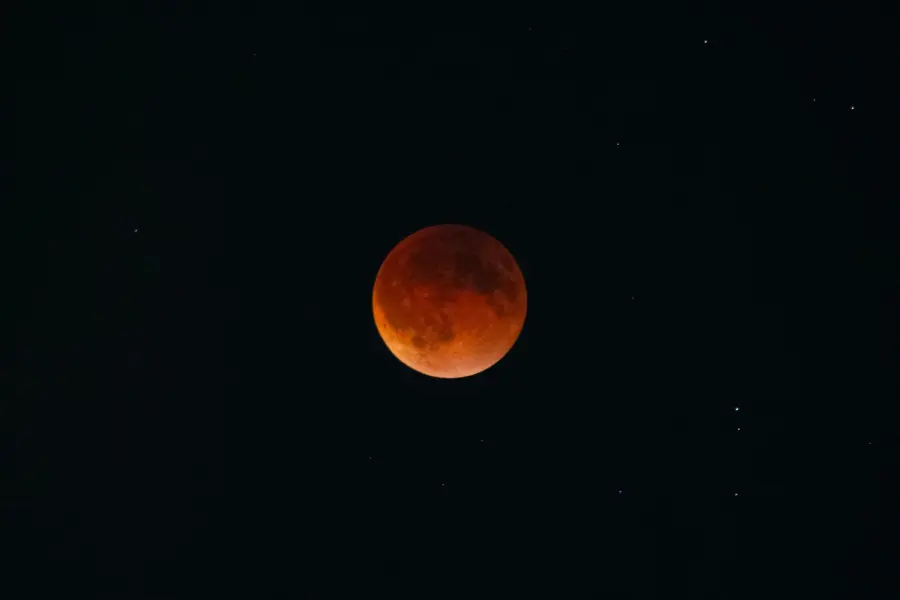 Capture of a blood moon during a lunar eclipse surrounded by stars in the night sky.