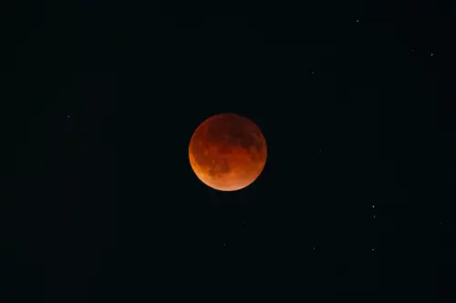 Capture of a blood moon during a lunar eclipse surrounded by stars in the night sky.