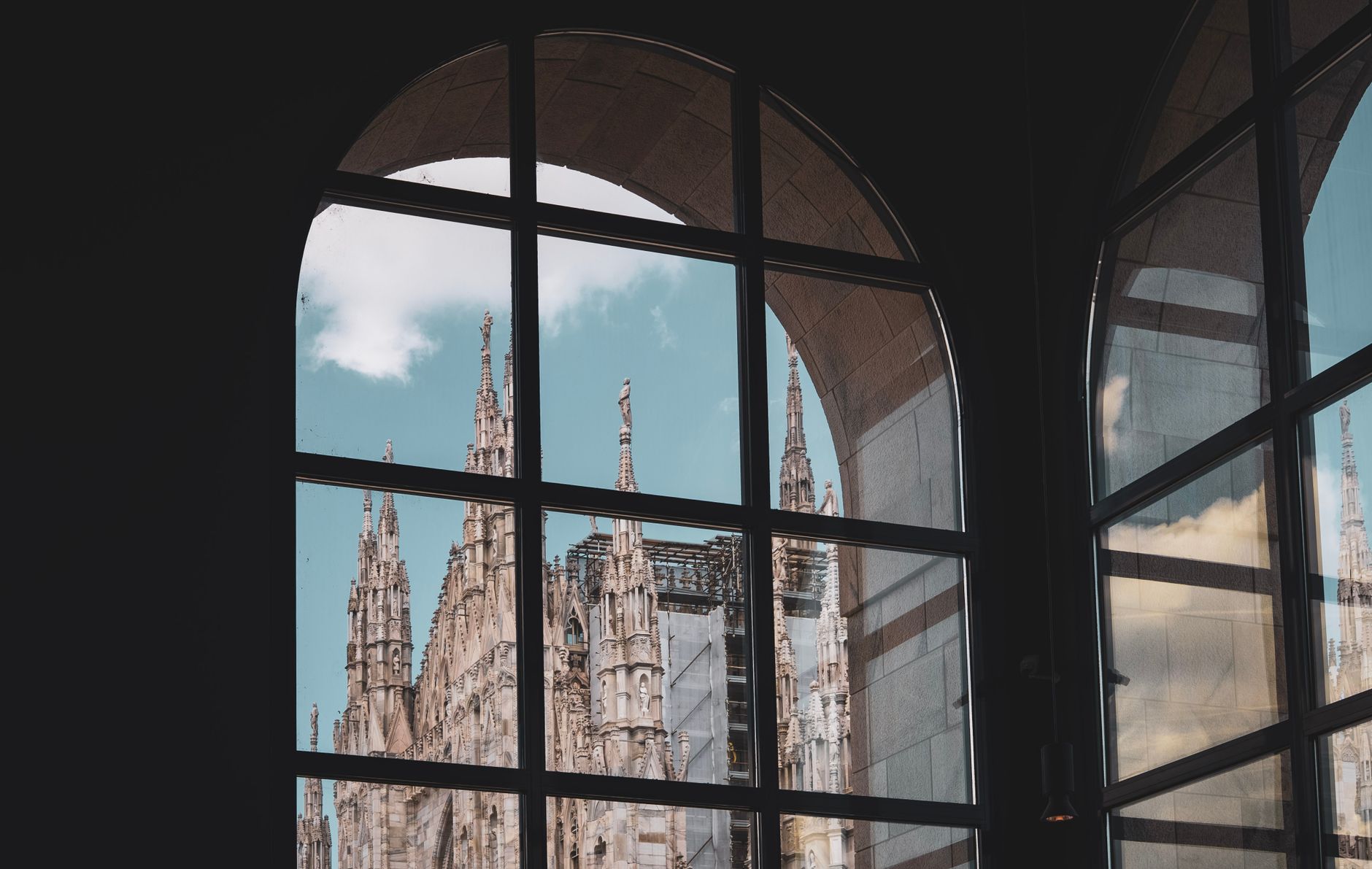 View of Duomo di Milano reflected in arched windows, showcasing iconic Gothic architecture.