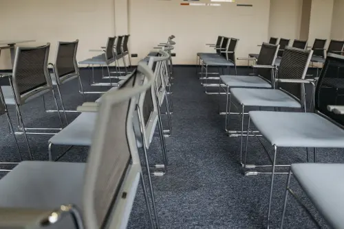 An empty meeting room with rows of modern chairs and carpet flooring, ready for use.