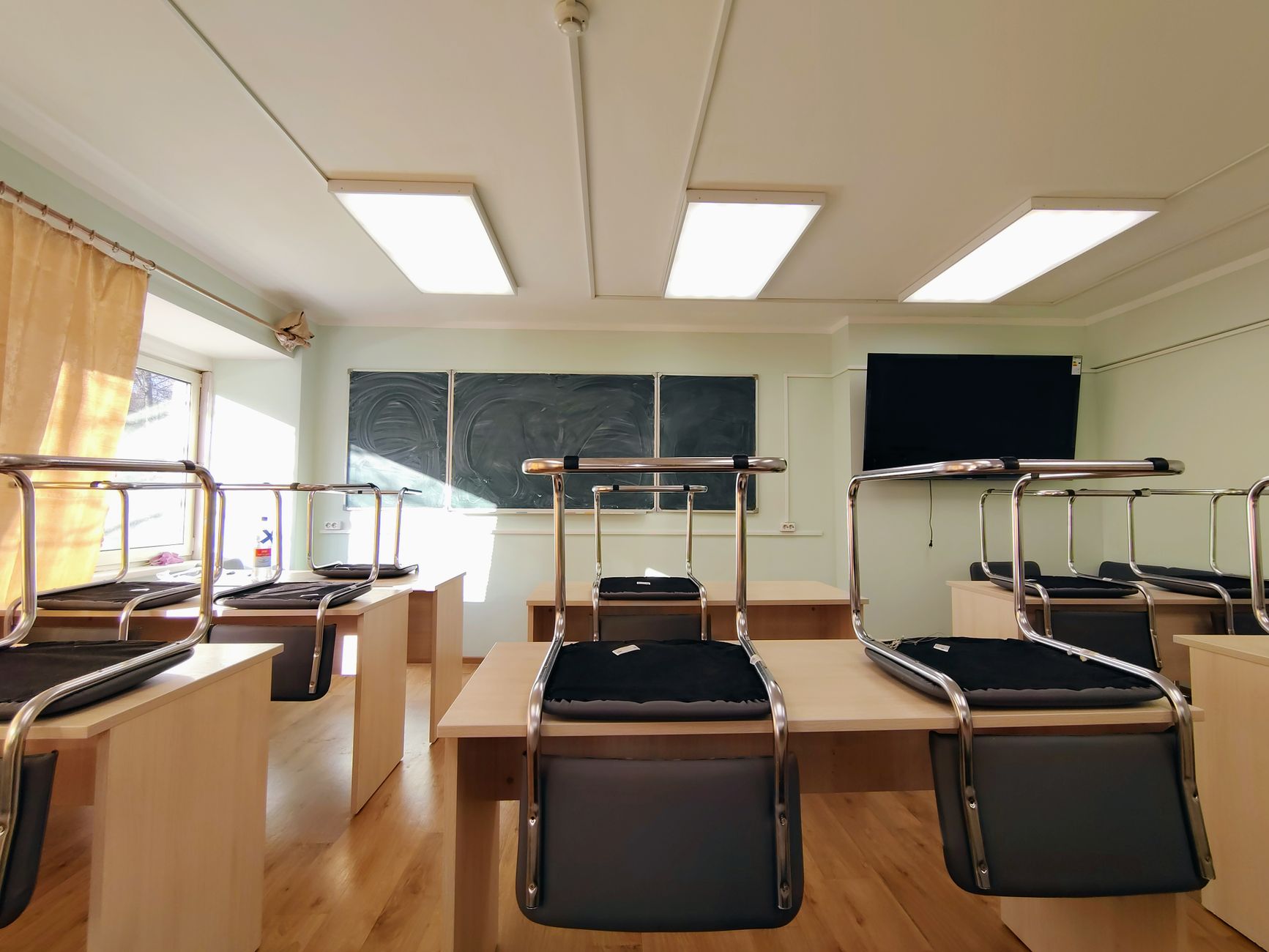 A wide view of an empty classroom with chairs stacked on desks and a blackboard in Moscow, Russia.