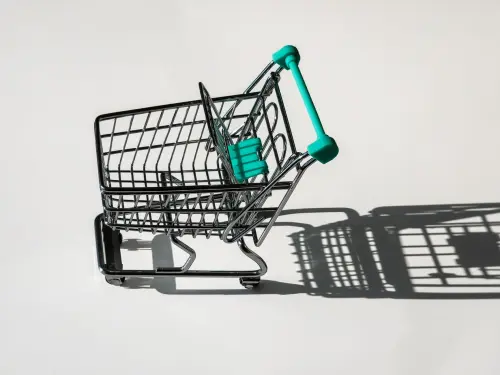 A close-up of a miniature shopping cart with teal accents casting a shadow on a white background.