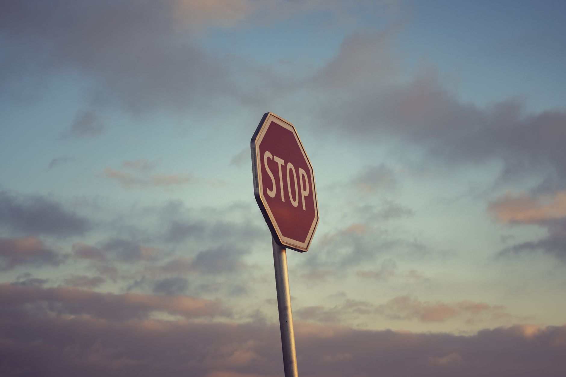 Moody stop sign silhouette against a scenic sunset sky with clouds.