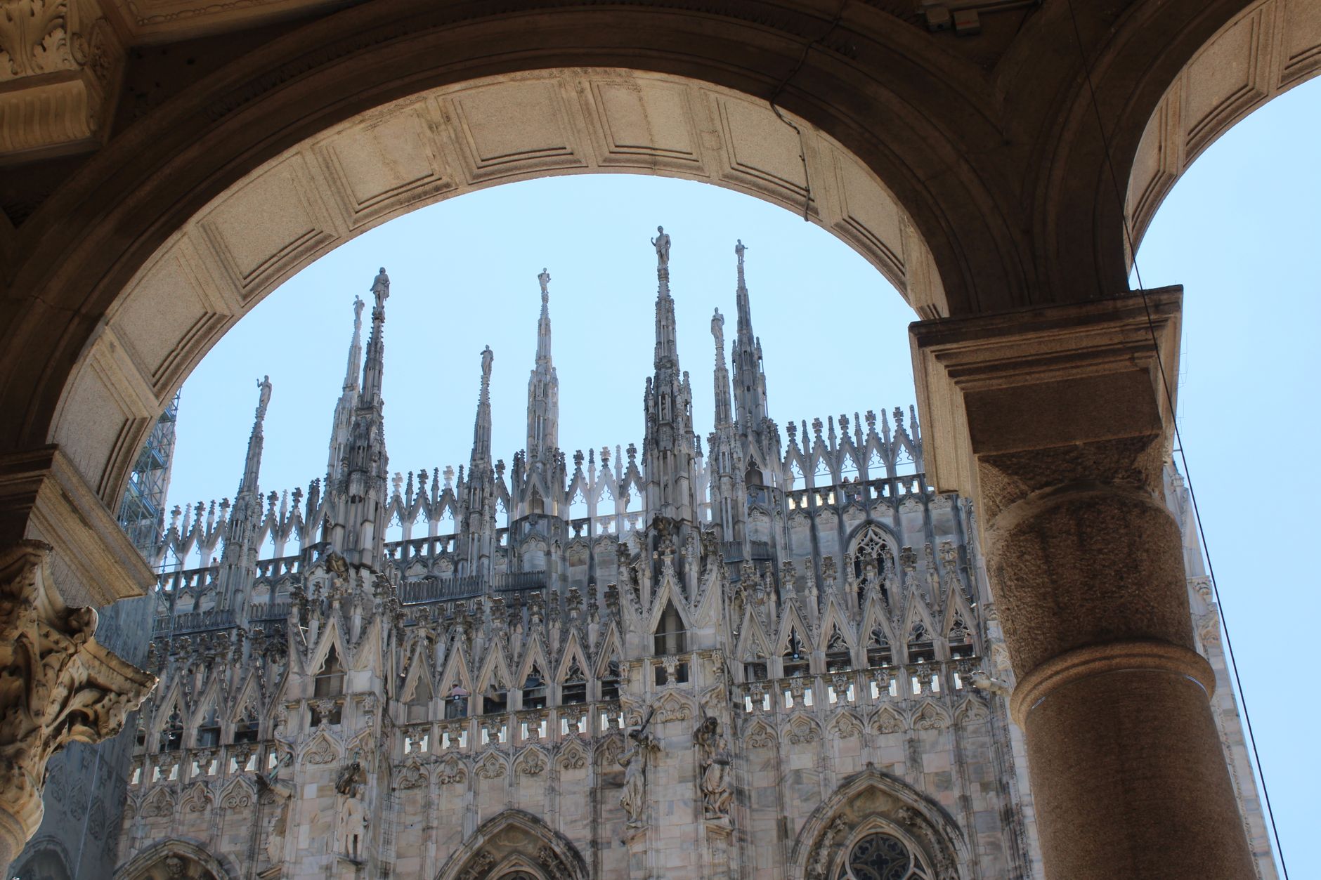 Gothic spires of the Milan Cathedral captured through an architectural archway in a sunny day.